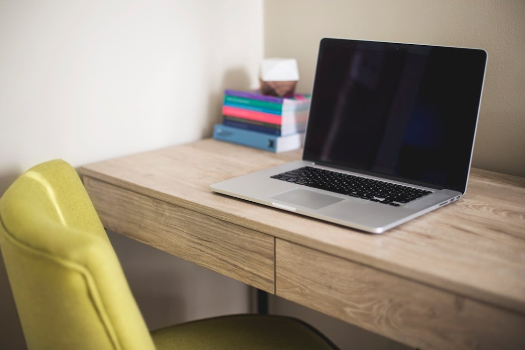 Laptop and books arranged on a small desk beside a window