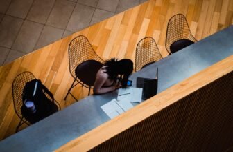 Person using a phone beside a laptop and paperwork at a quiet workspace